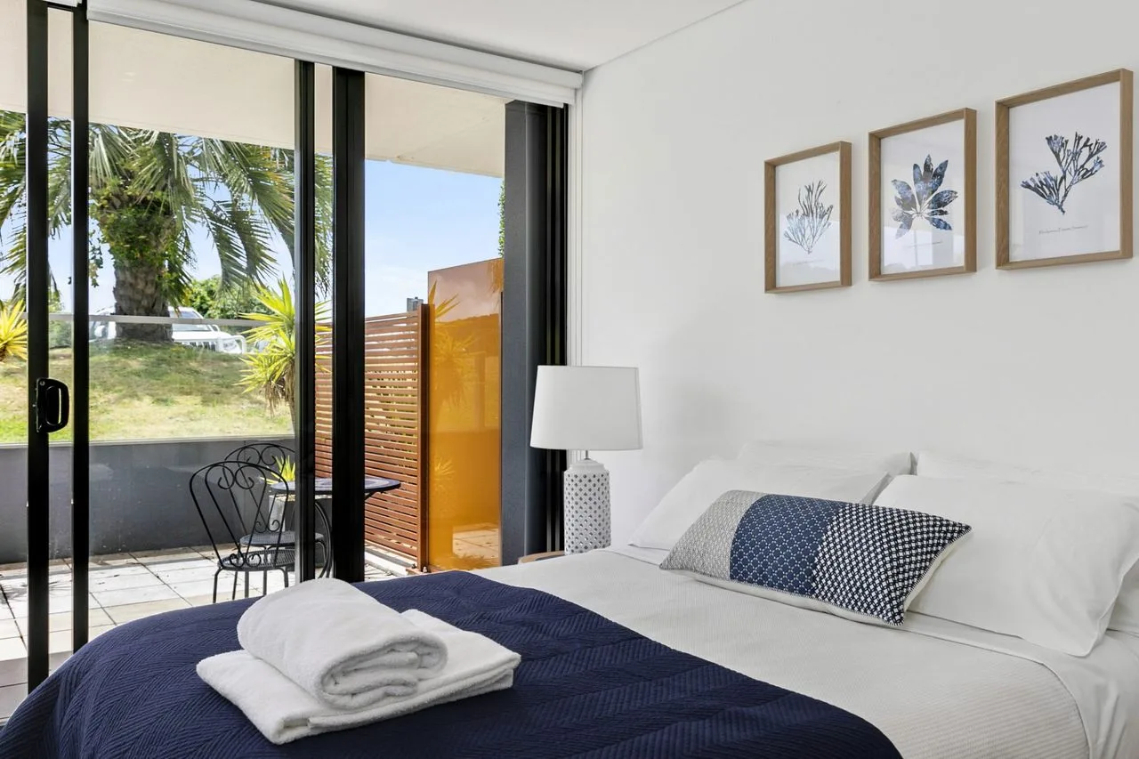 Un dormitorio luminoso con una cama bien arreglada junto a grandes puertas de vidrio.