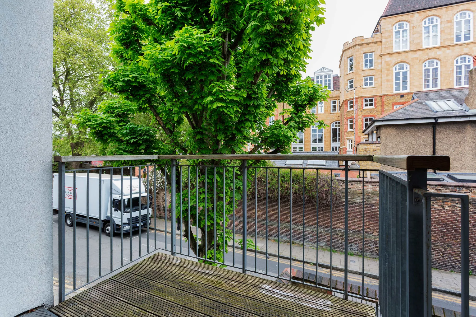 A small balcony overlooks a leafy courtyard and nearby brick buildings.