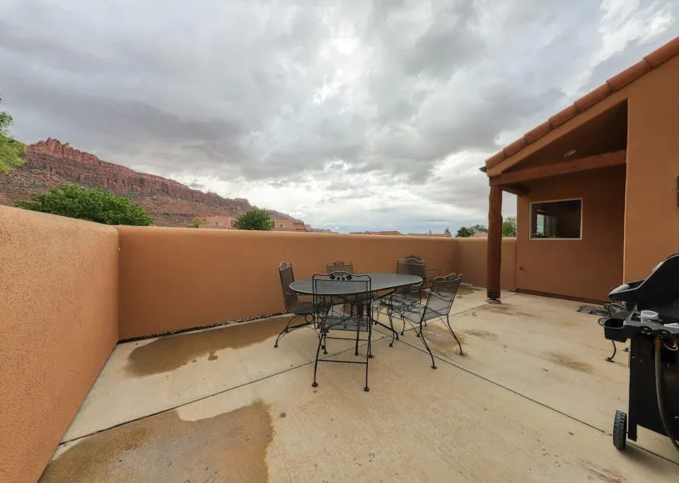 Un patio al aire libre con una mesa y asientos junto a un área cubierta.