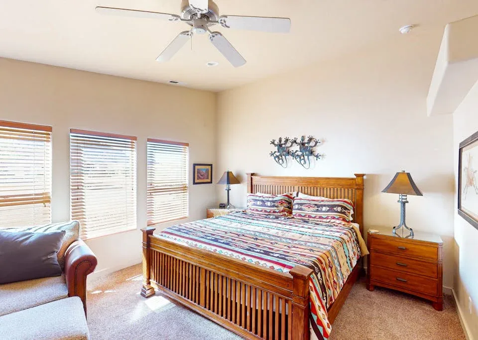 Un dormitorio con una cama de madera, ropa de cama colorida y ventanas con persianas.