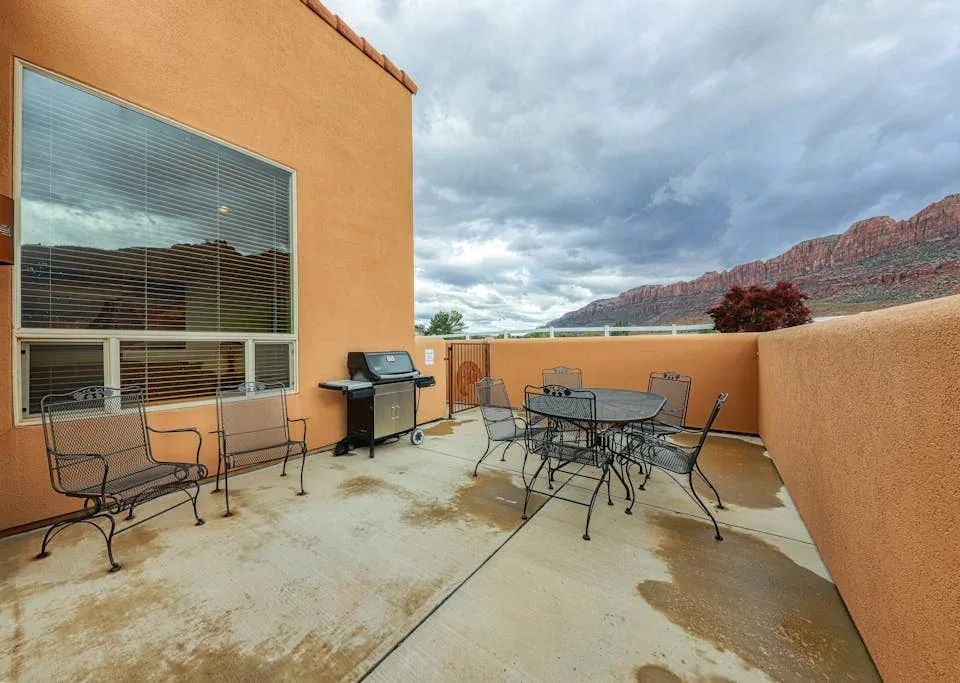 Un patio exterior con mesa, asientos y una barbacoa junto a un edificio naranja.