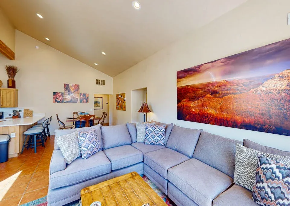 Una sala de estar con un sofá seccional y una gran obra de paisaje en la pared.