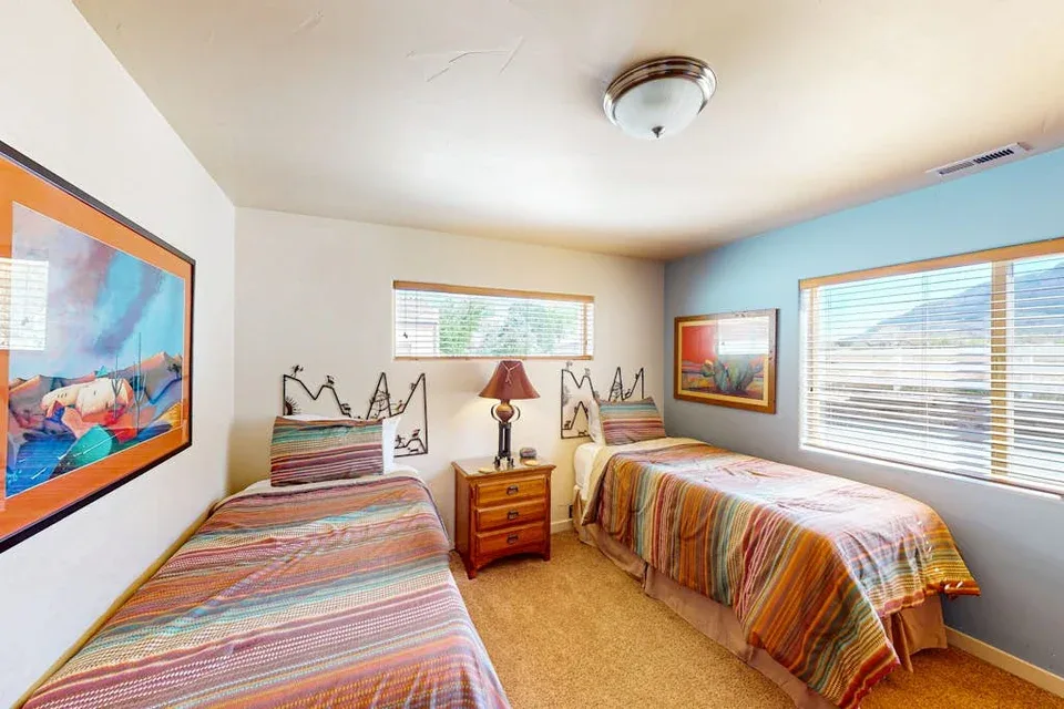 Un dormitorio con dos camas, una mesita de noche y ventanas con persianas.