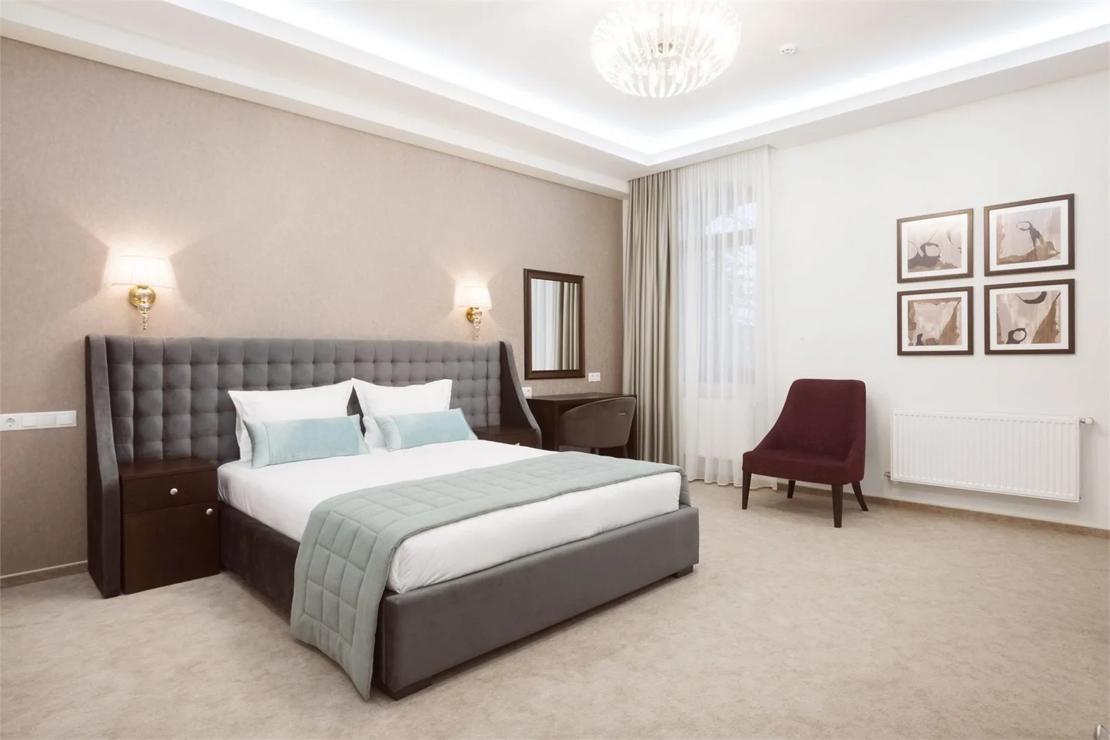 Espacio representativo del hotel: Un dormitorio con una cama grande, un escritorio y una silla color burdeos.