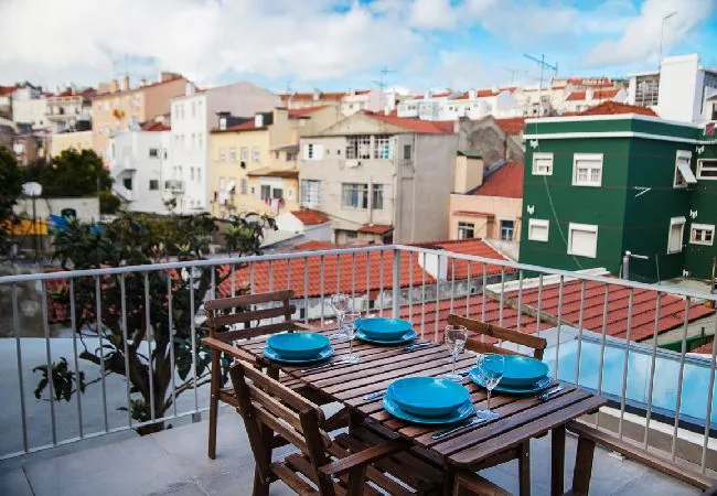 A rooftop terrace has a wooden dining table set with blue plates, overlooking nearby buildings.