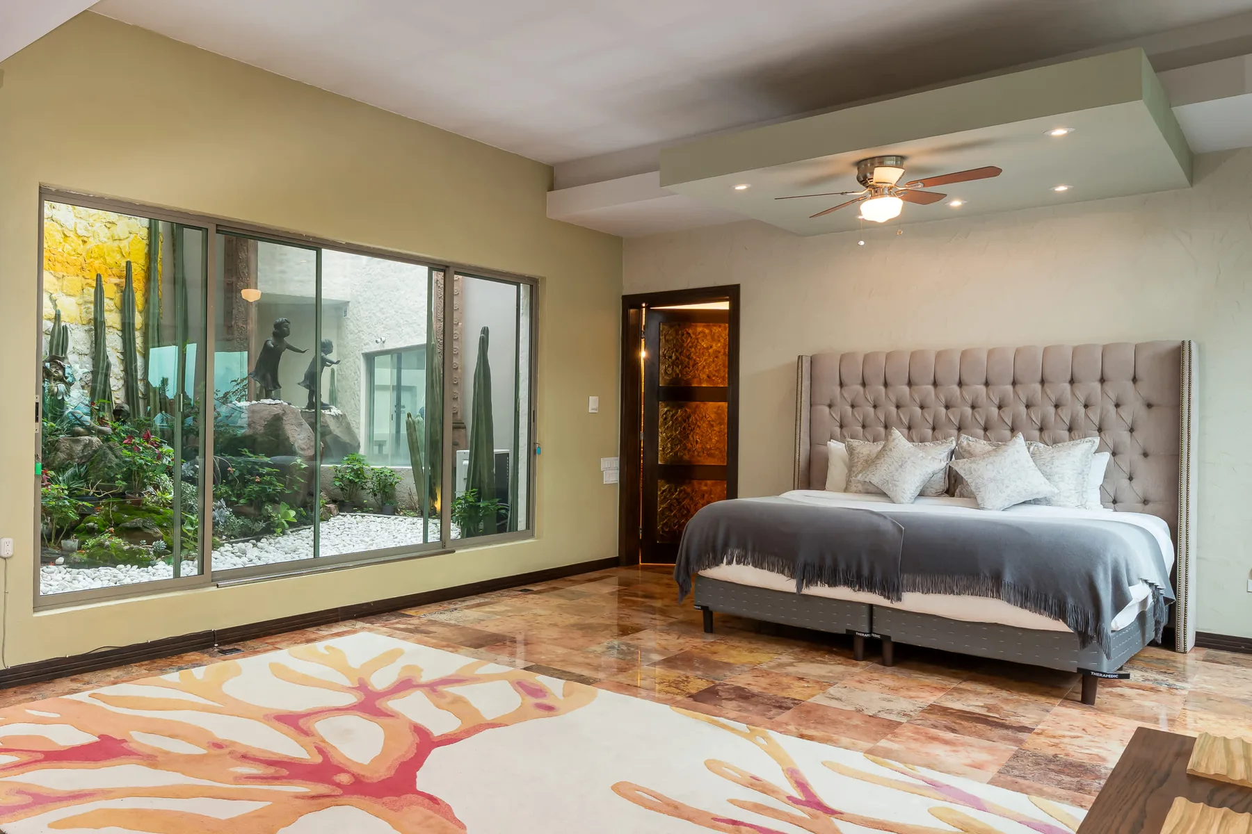 A bedroom with a large bed and windows overlooking a landscaped courtyard.