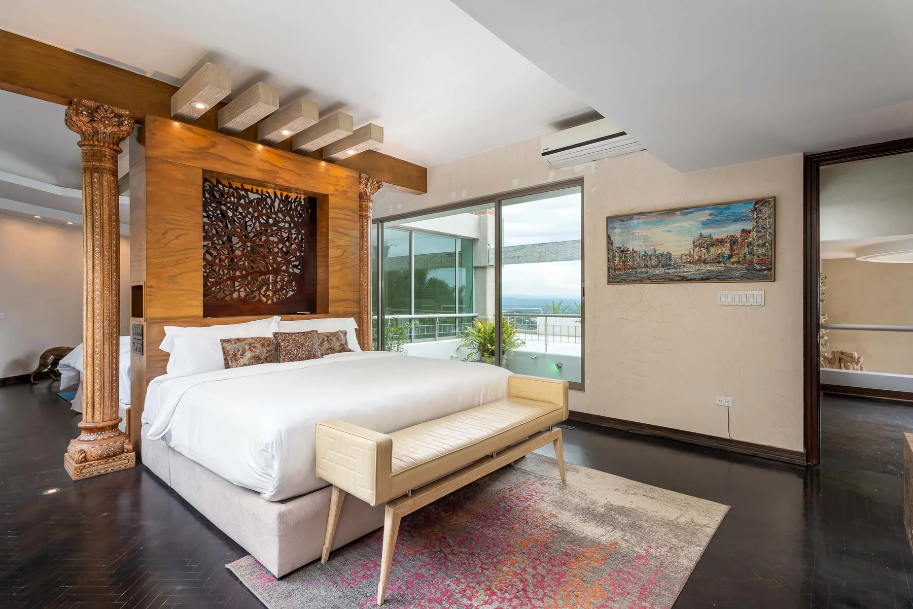 A bedroom with a large bed, a bench, and glass doors opening to a balcony.