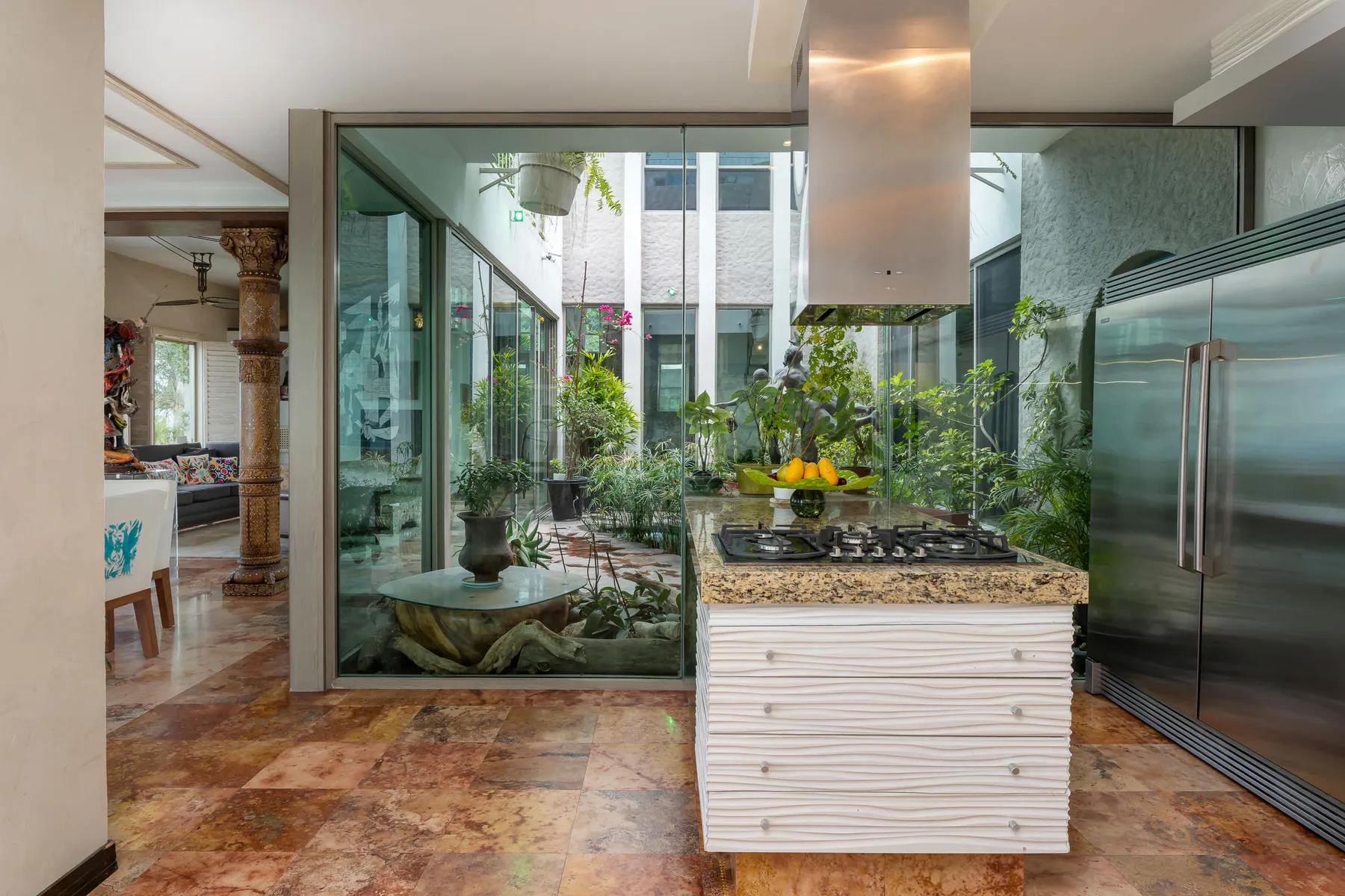 A modern kitchen opens onto a glass-enclosed courtyard with greenery.