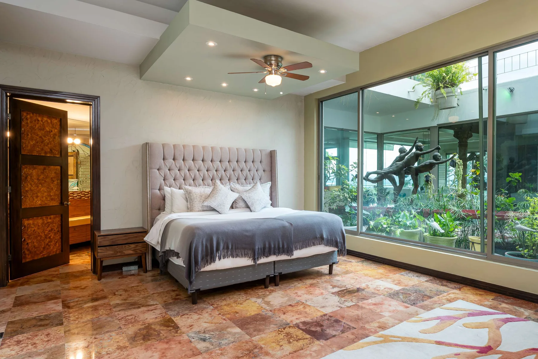 A bedroom with a bed beside large windows overlooking a garden.