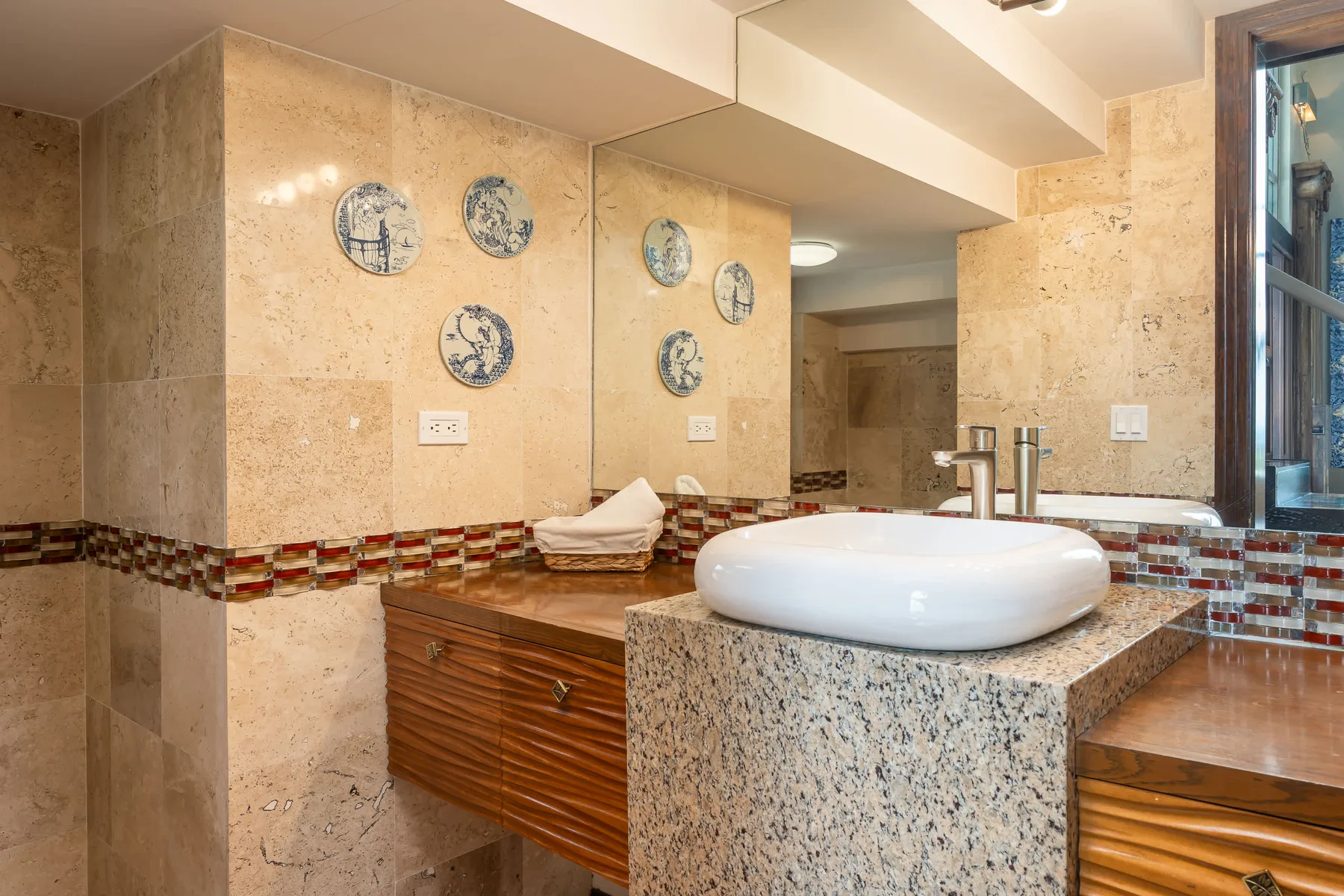 A bathroom vanity with a white vessel sink, stone counter, and decorative wall tiles.