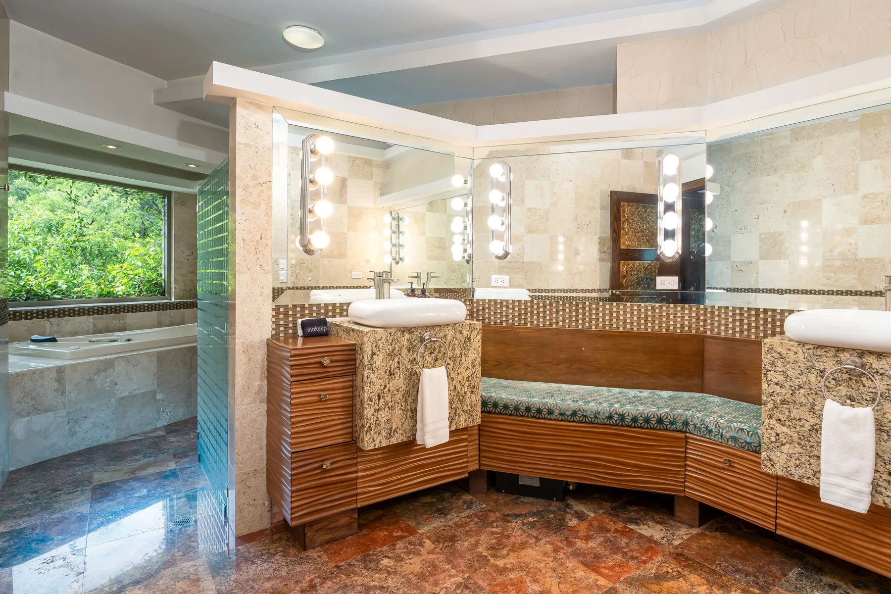 A spacious bathroom with a long vanity, mirrors, and a bathtub by the window.