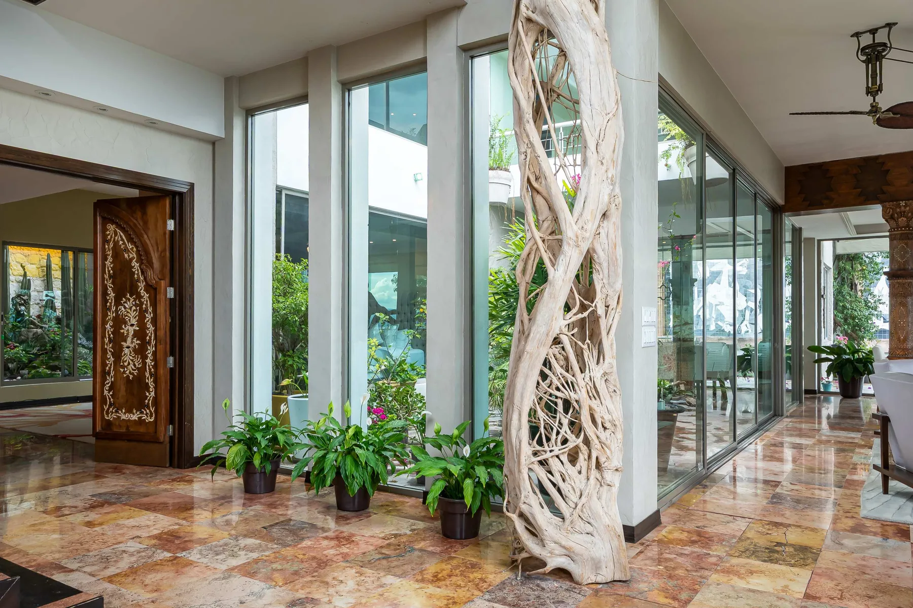 A bright glass-walled interior opens onto a lush garden, with plants beside the windows.