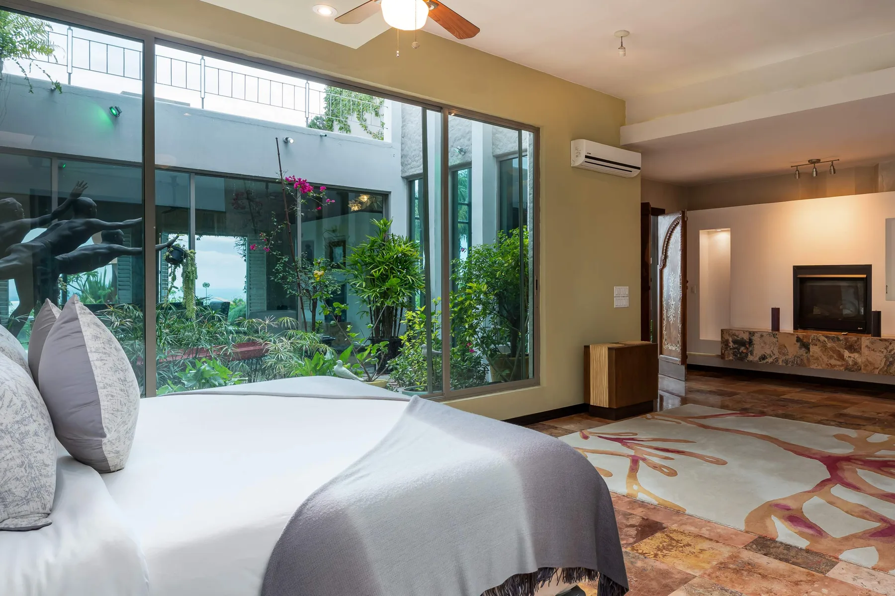 A bedroom with a bed beside large windows overlooking a garden.