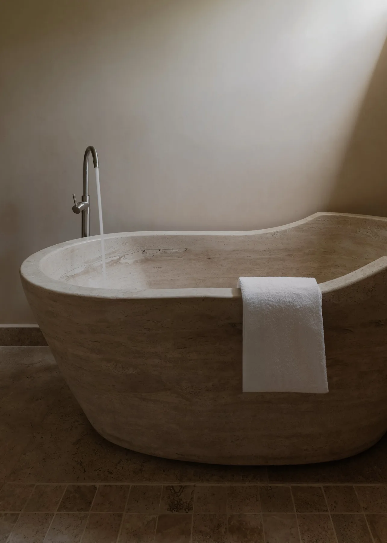 Una bañera exenta está junto a una pared lisa, con una toalla sobre el borde.