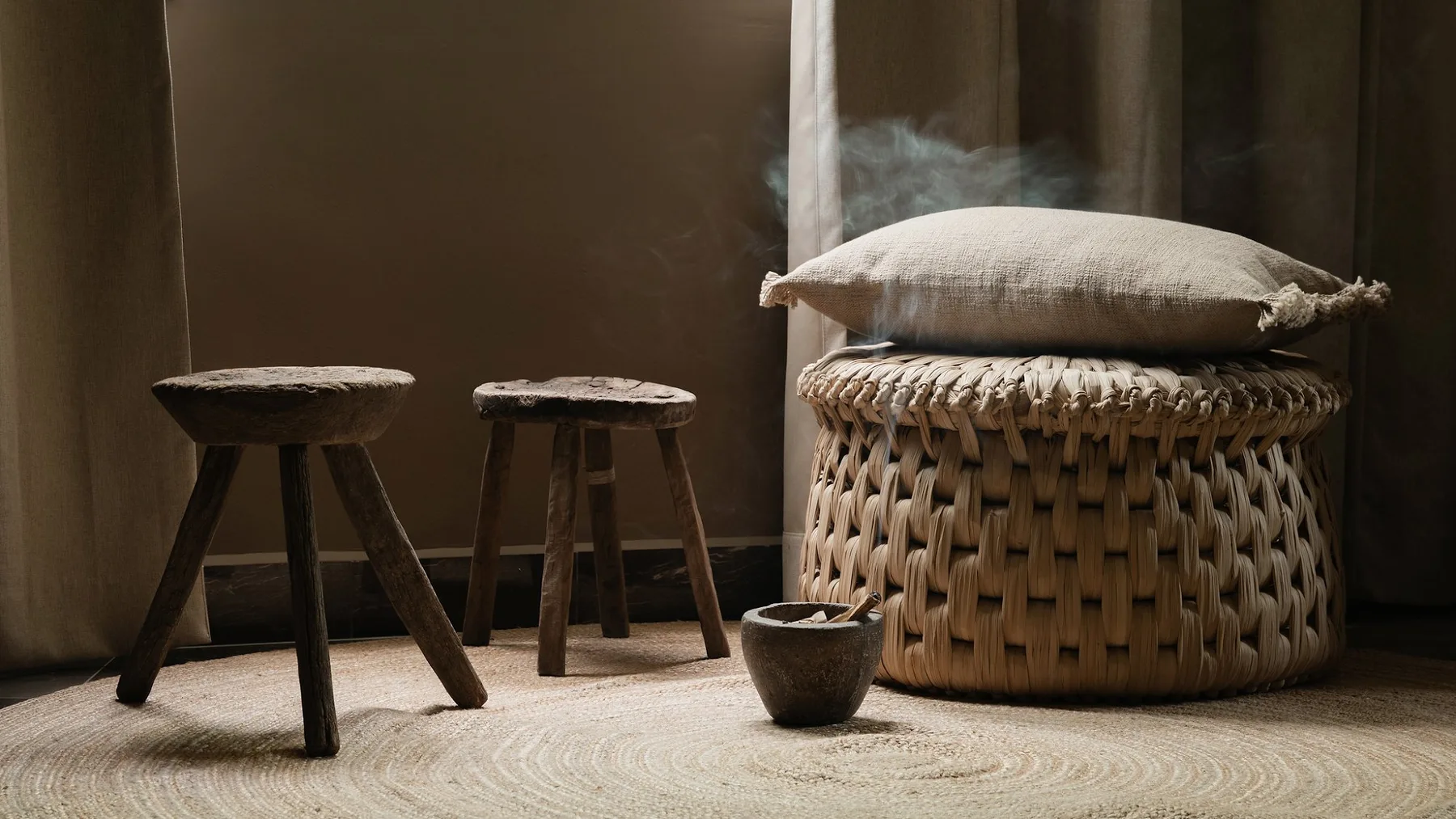 Un asiento tejido con cojín está junto a dos pequeños taburetes de madera.
