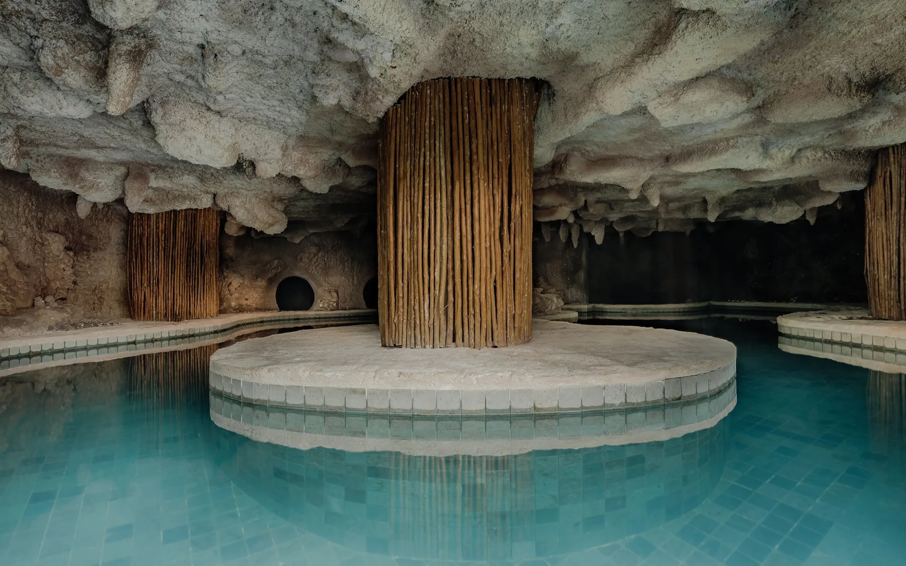 Zona común: Una piscina interior bajo un techo rocoso, con una plataforma circular en el centro.