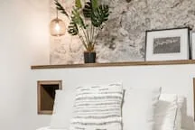 A bedroom with a bed, striped pillows, and a leafy plant on a shelf.