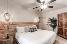 A bedroom with a neatly made bed, wooden headboard, and ceiling fan.