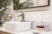 A bathroom vanity with a white vessel sink, bronze faucet, and toiletries.