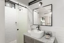 A bathroom with a glass shower, a sink, and a wall mirror.