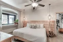 A bright bedroom with a bed beneath a ceiling fan and a large window.