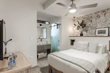 A bright bedroom with a neatly made bed and a stone accent wall.