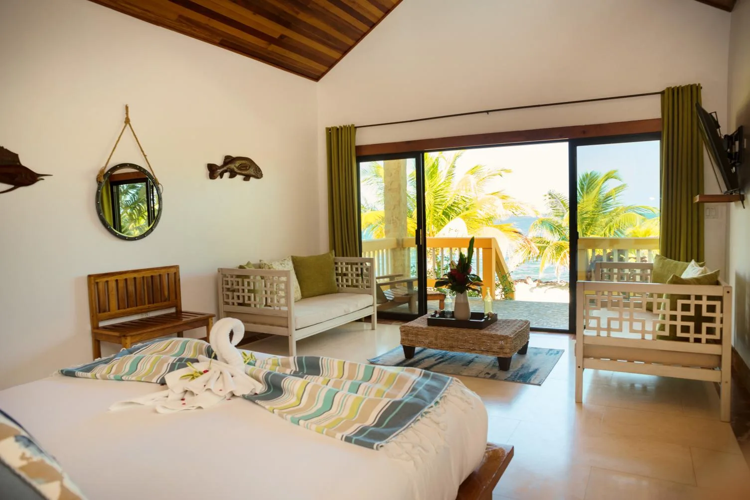 A bright bedroom with a bed, seating, and glass doors opening onto a palm-lined view.