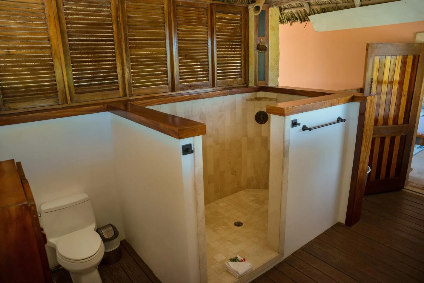 A bathroom with a tiled shower area and toilet beside wooden shutters.