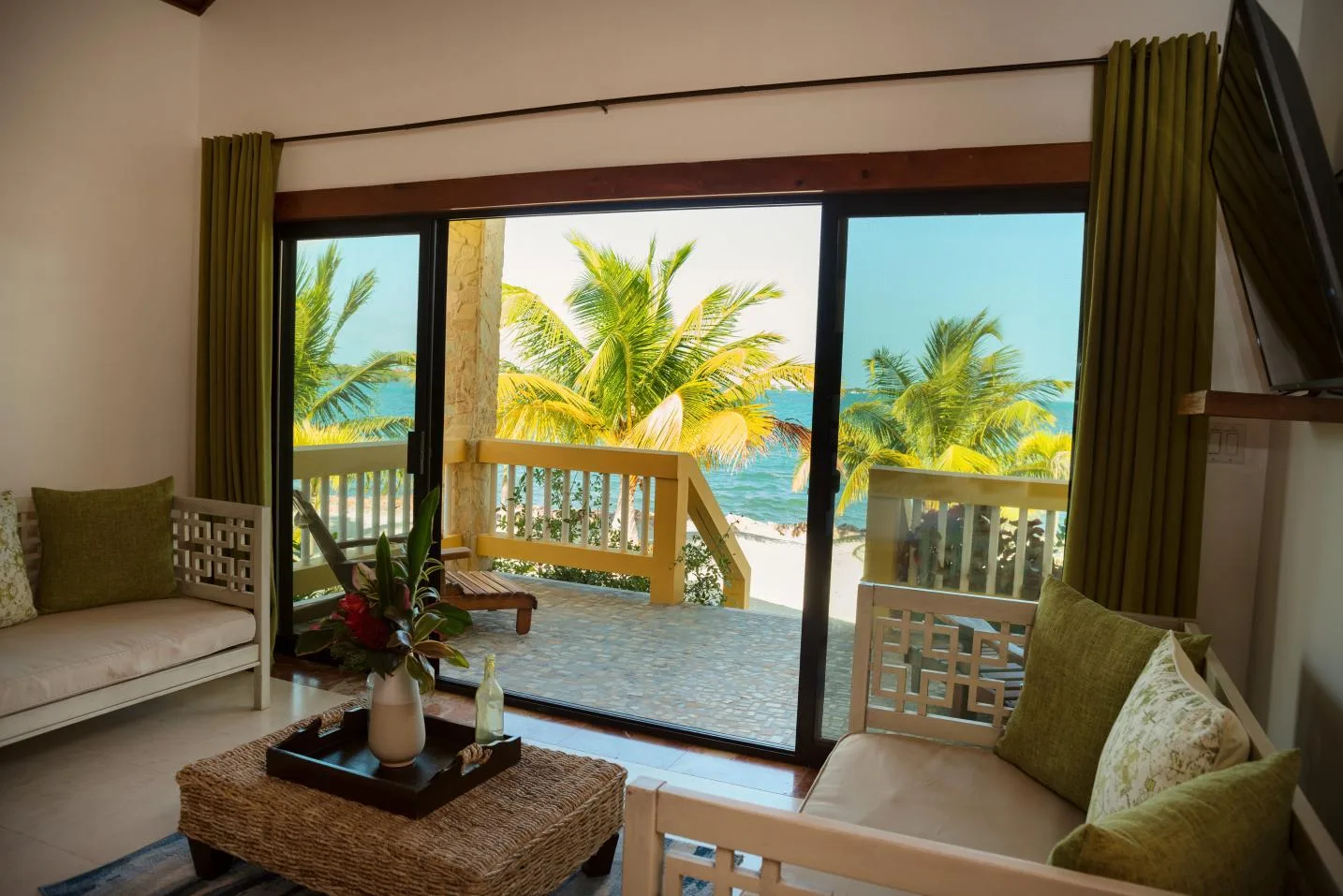 A living area opens through sliding glass doors onto a balcony overlooking palm trees and the sea.