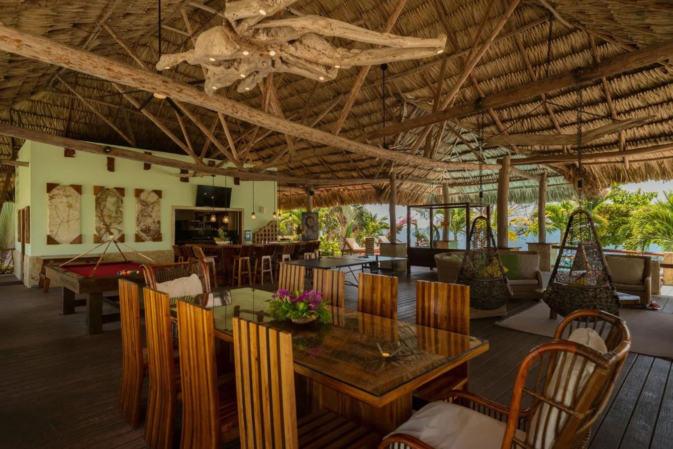 An open-air dining and lounge area has wooden seating beneath a thatched roof.