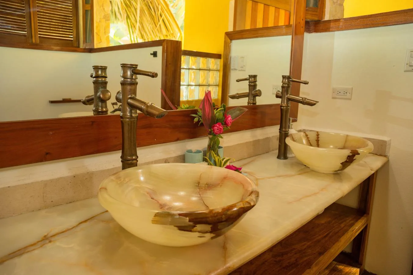 A bathroom vanity with two vessel sinks, tall faucets, and a flower arrangement.