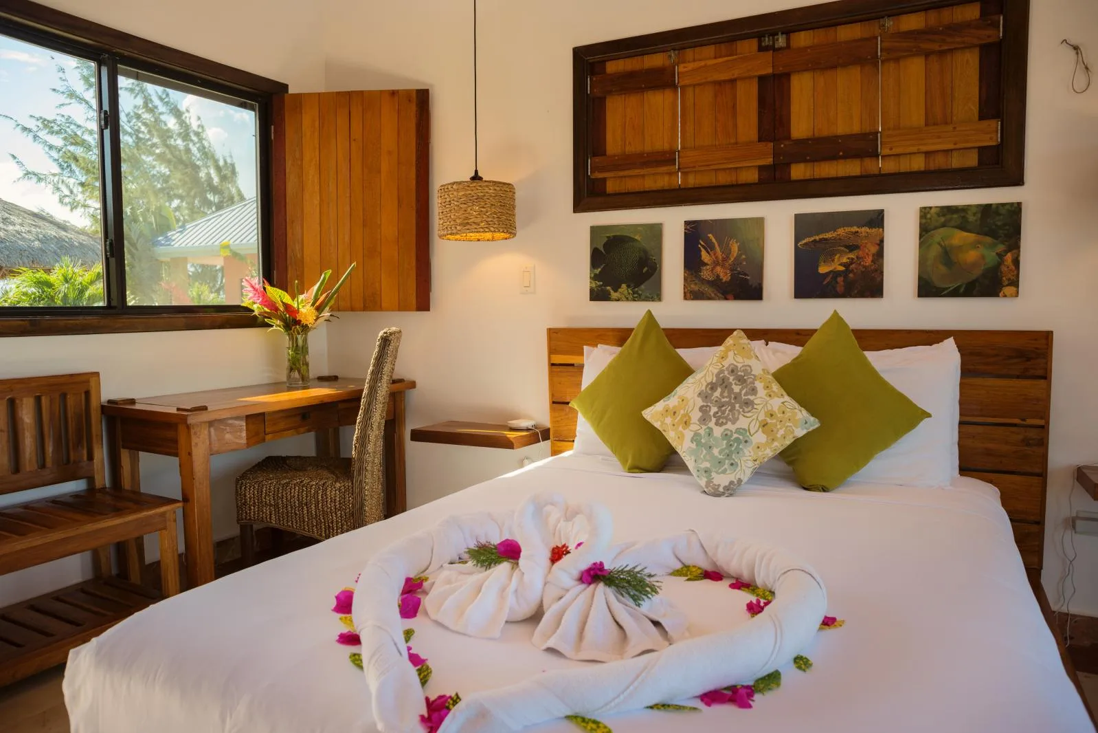 A bedroom with a white bed, green pillows, and a wooden desk beside the window.