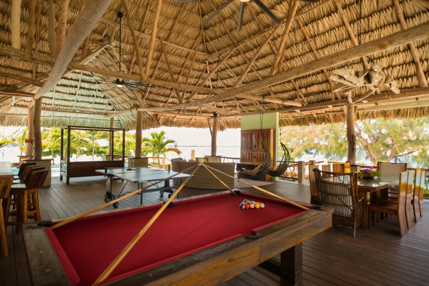 An open-air thatched pavilion has a red-felt billiards table and dining seating.