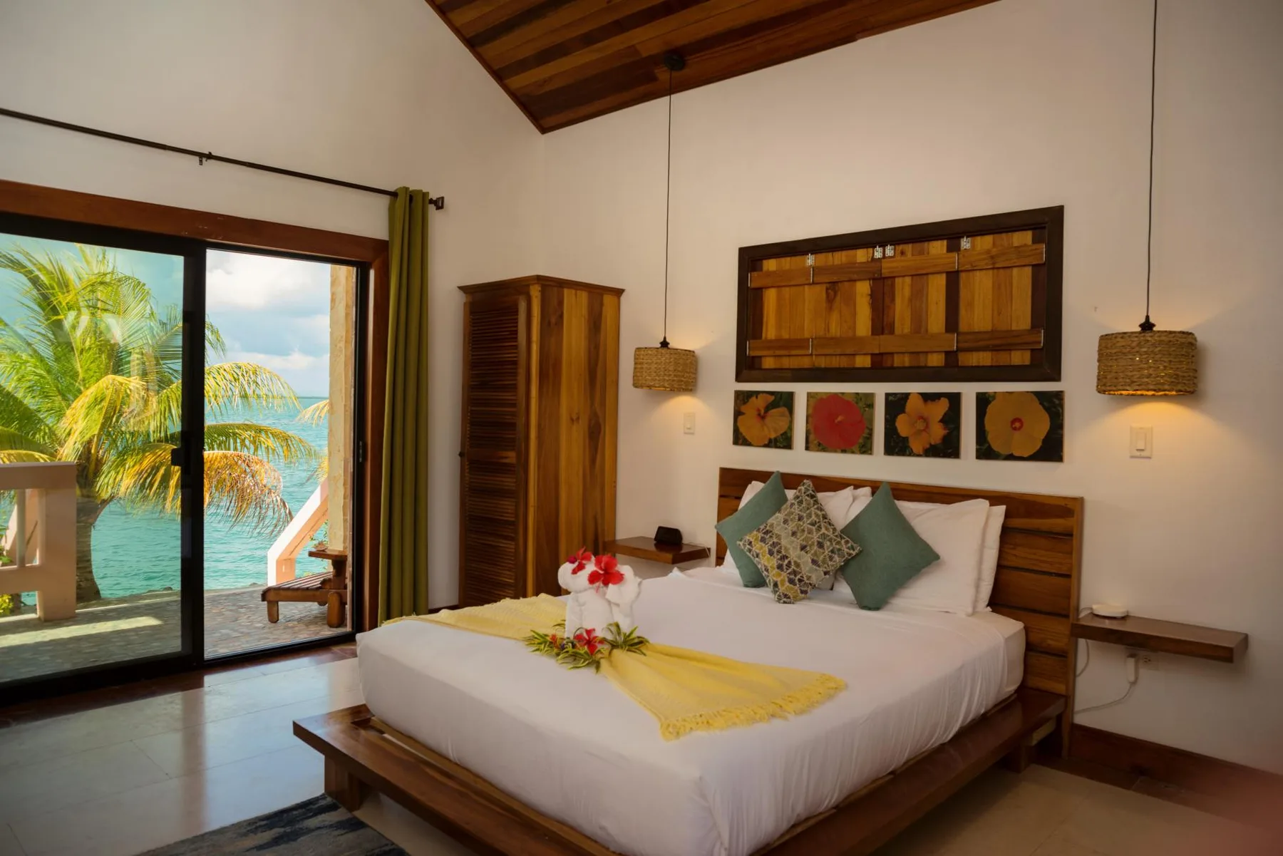 A bedroom with a neatly made bed and sliding glass doors opening to a tropical view.