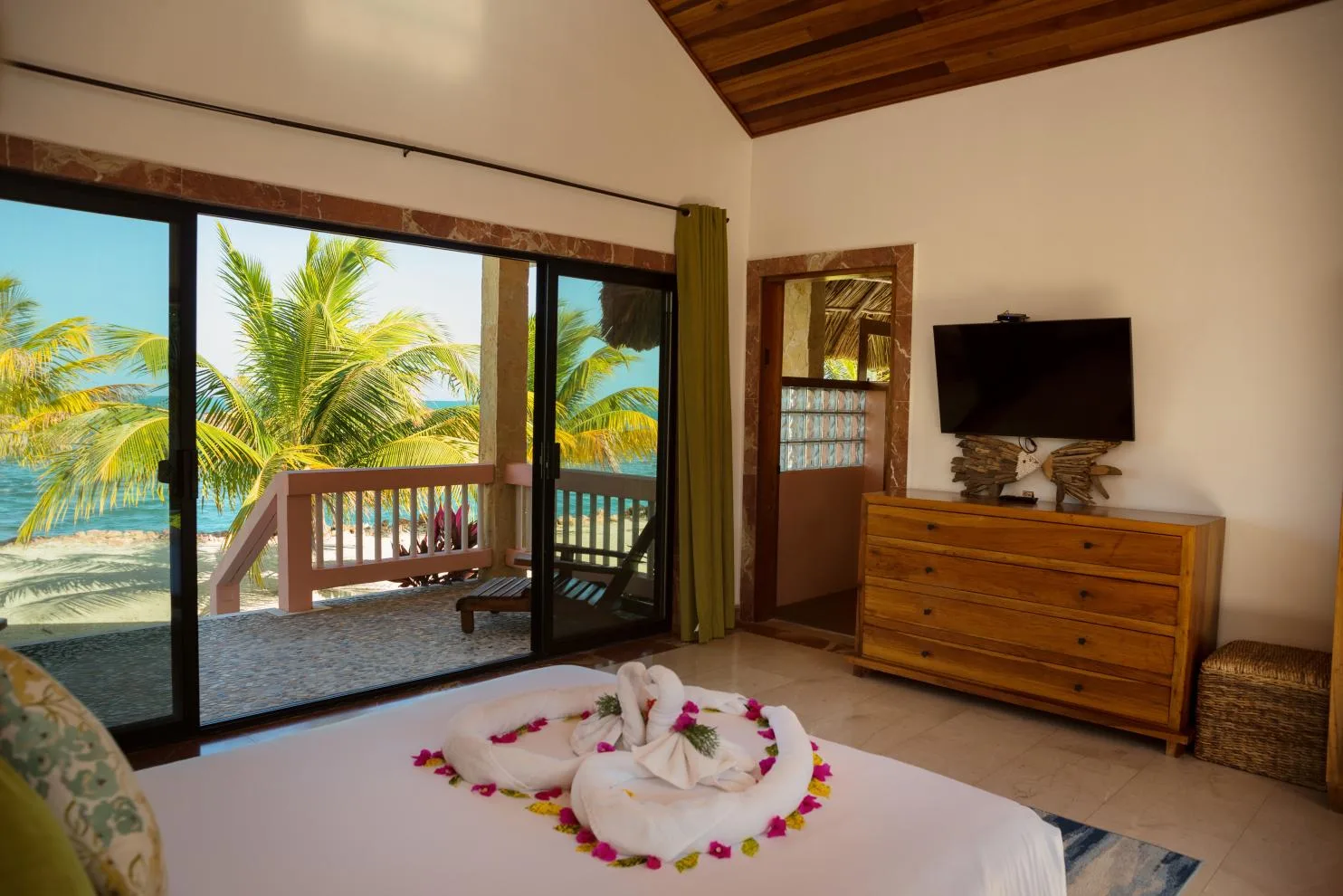 A bedroom opens onto a balcony with palm trees and a view of the water.