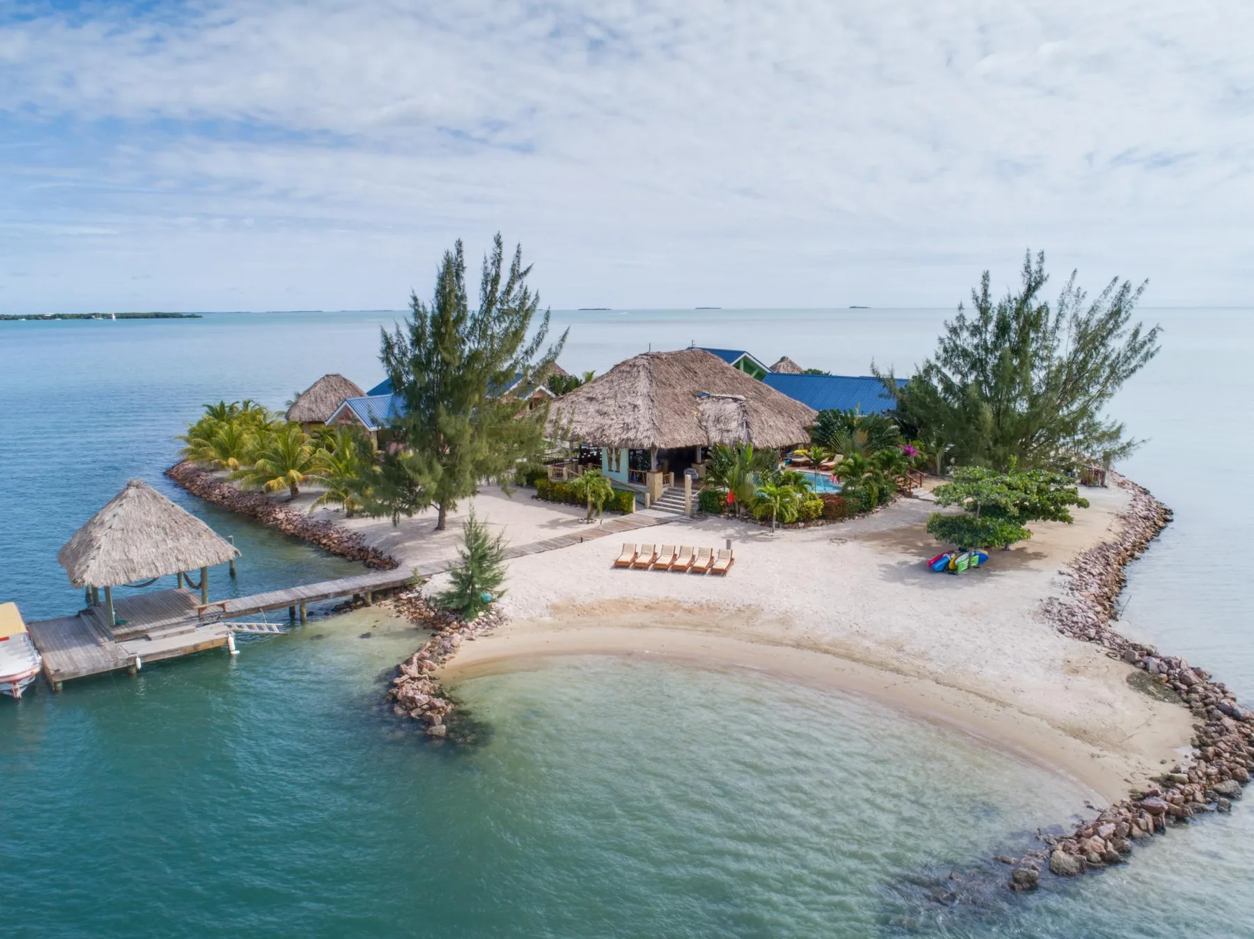 A small sandy island with thatched structures, trees, and surrounding turquoise water.