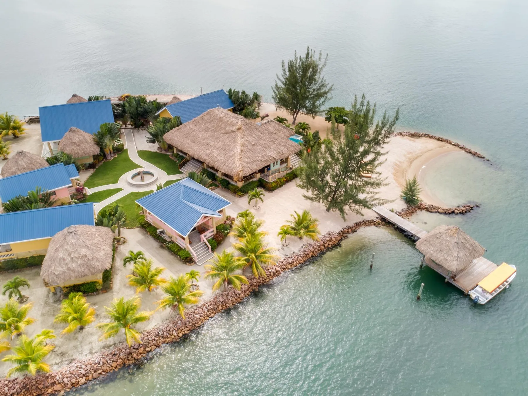 Aerial view of a tropical waterfront resort with thatched-roof buildings and a small pier.
