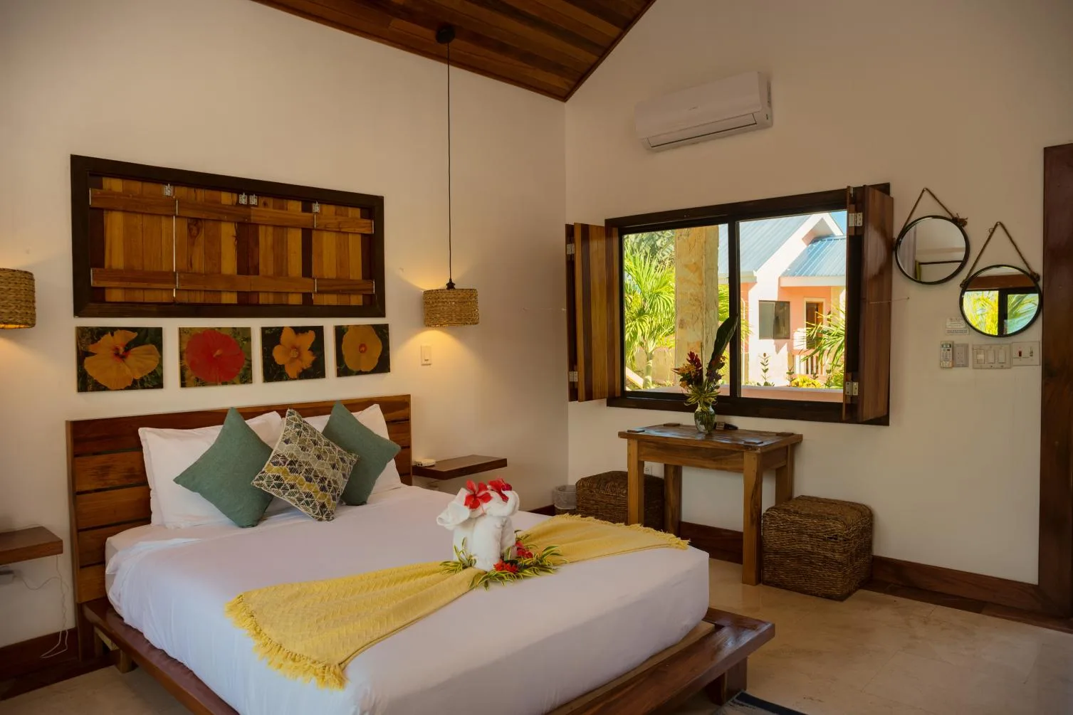 A bedroom with a double bed, colorful cushions, and a window overlooking greenery.