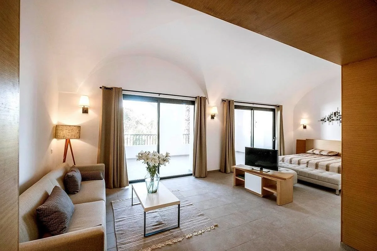 Espacio representativo del hotel: Una luminosa sala de estar con asientos, televisor y grandes ventanas junto a una cama.