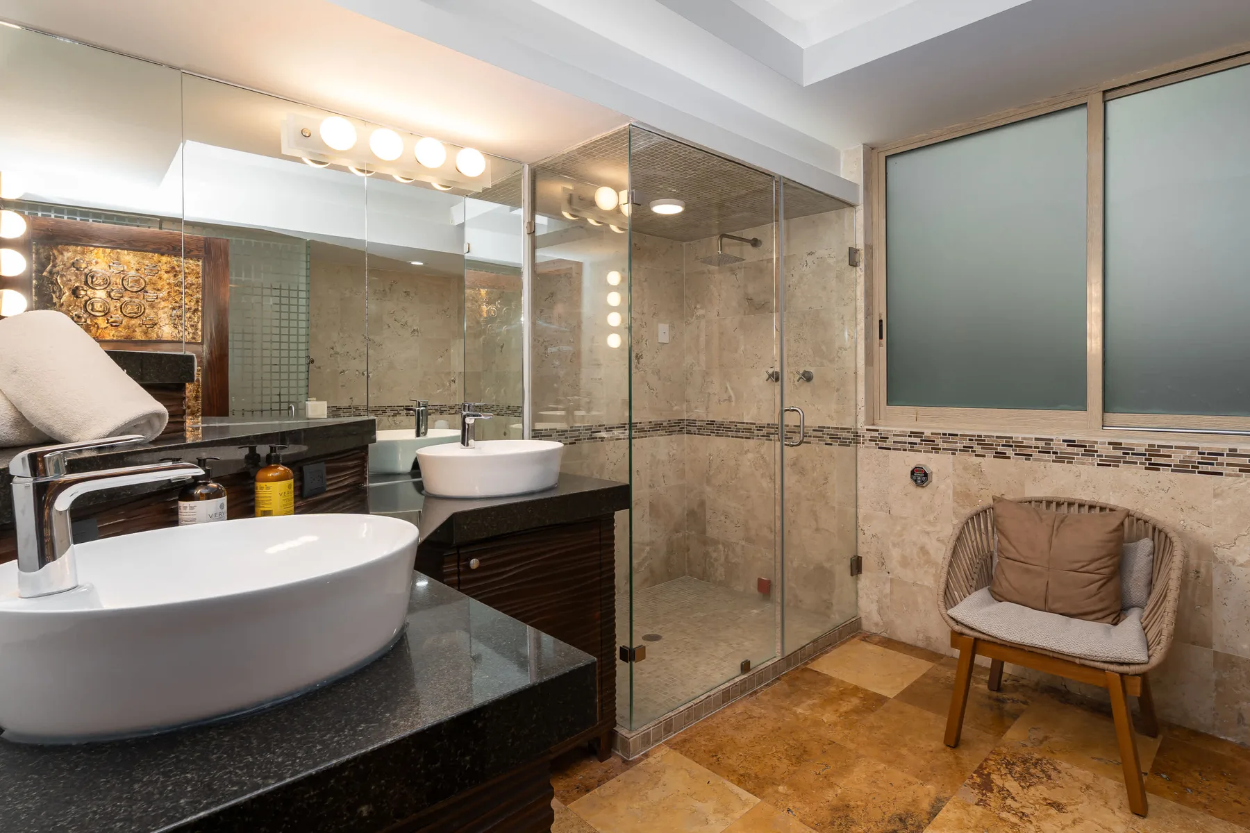 Un baño con ducha de vidrio, lavabo sobre encimera y asiento acolchado.