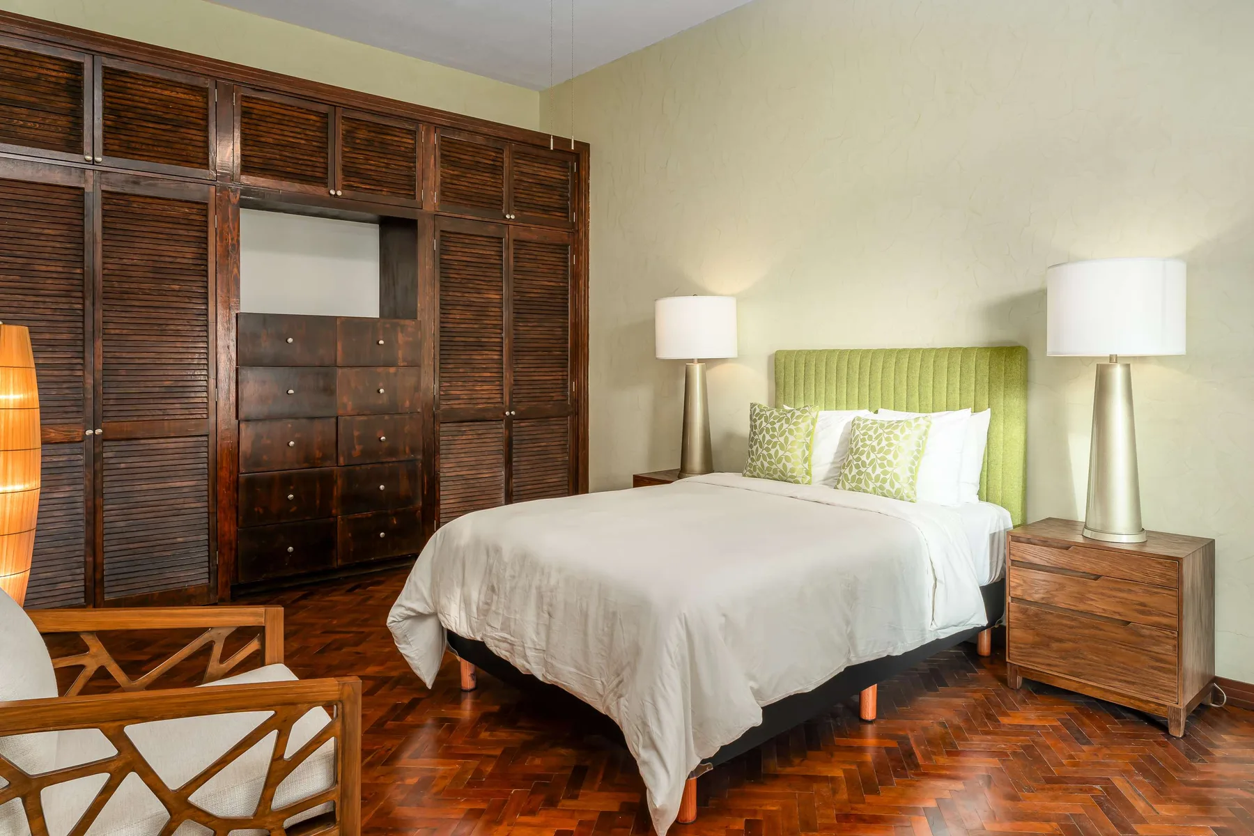 Un dormitorio con cama, cabecero verde y armarios de madera.