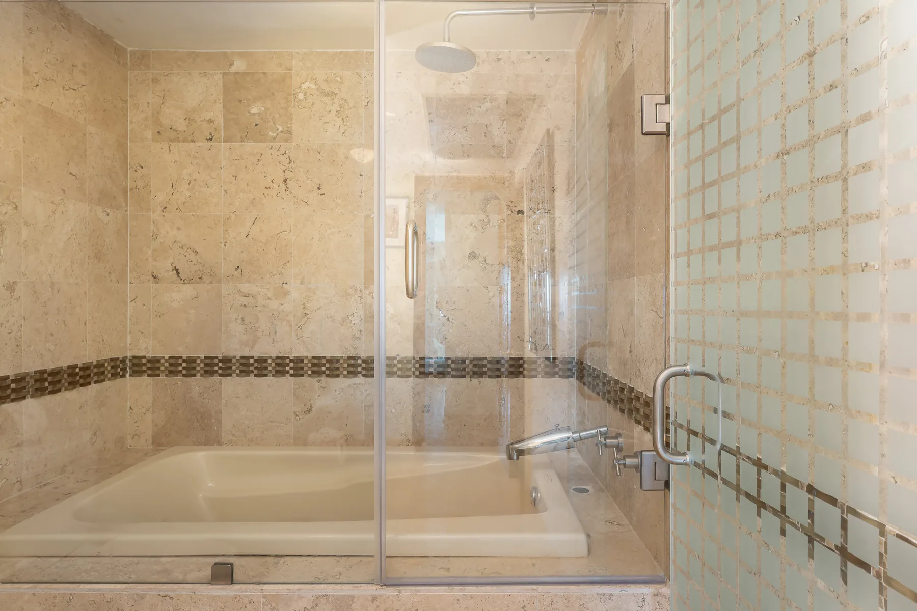 Un baño con bañera, mampara de vidrio y paredes revestidas de azulejos.