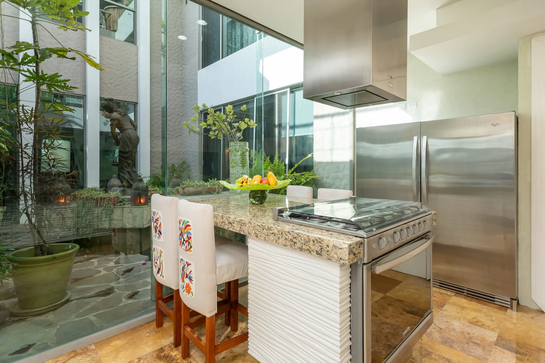 Una cocina moderna con una isla central, una placa de cocción y taburetes junto a un patio acristalado.