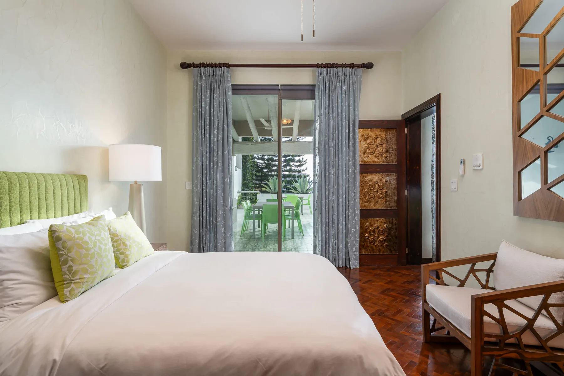 Un dormitorio con una cama grande, cortinas grises y una puerta de vidrio que da a un patio.