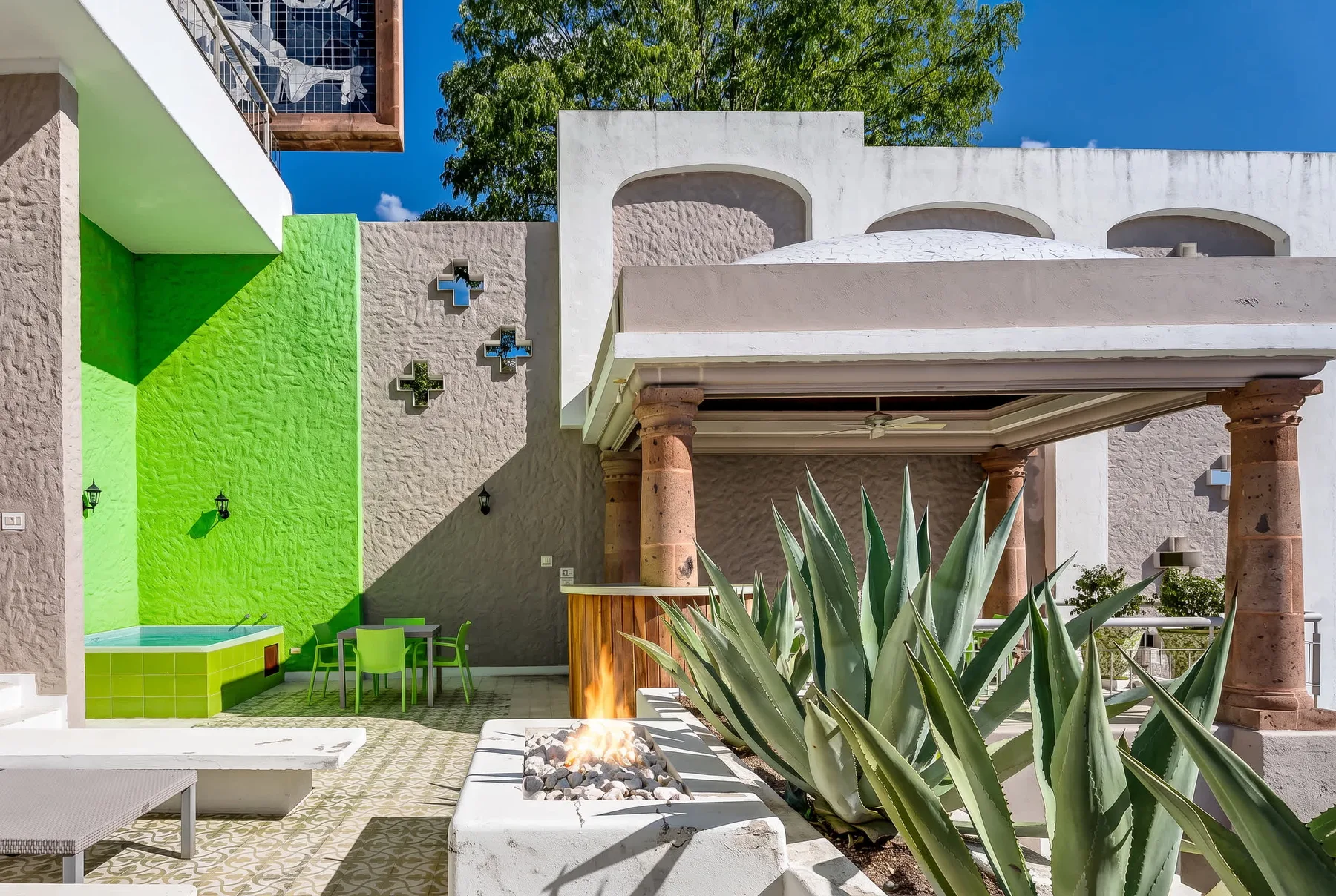 Un patio al aire libre con una zona de estar cubierta, paredes coloridas y grandes plantas de agave.