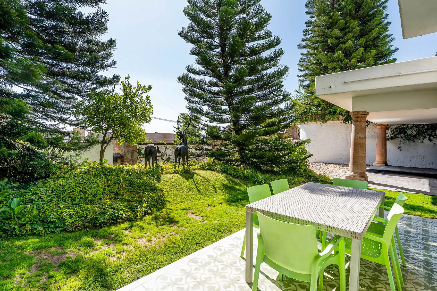 Un patio exterior con una mesa y sillas verdes da a un jardín frondoso.
