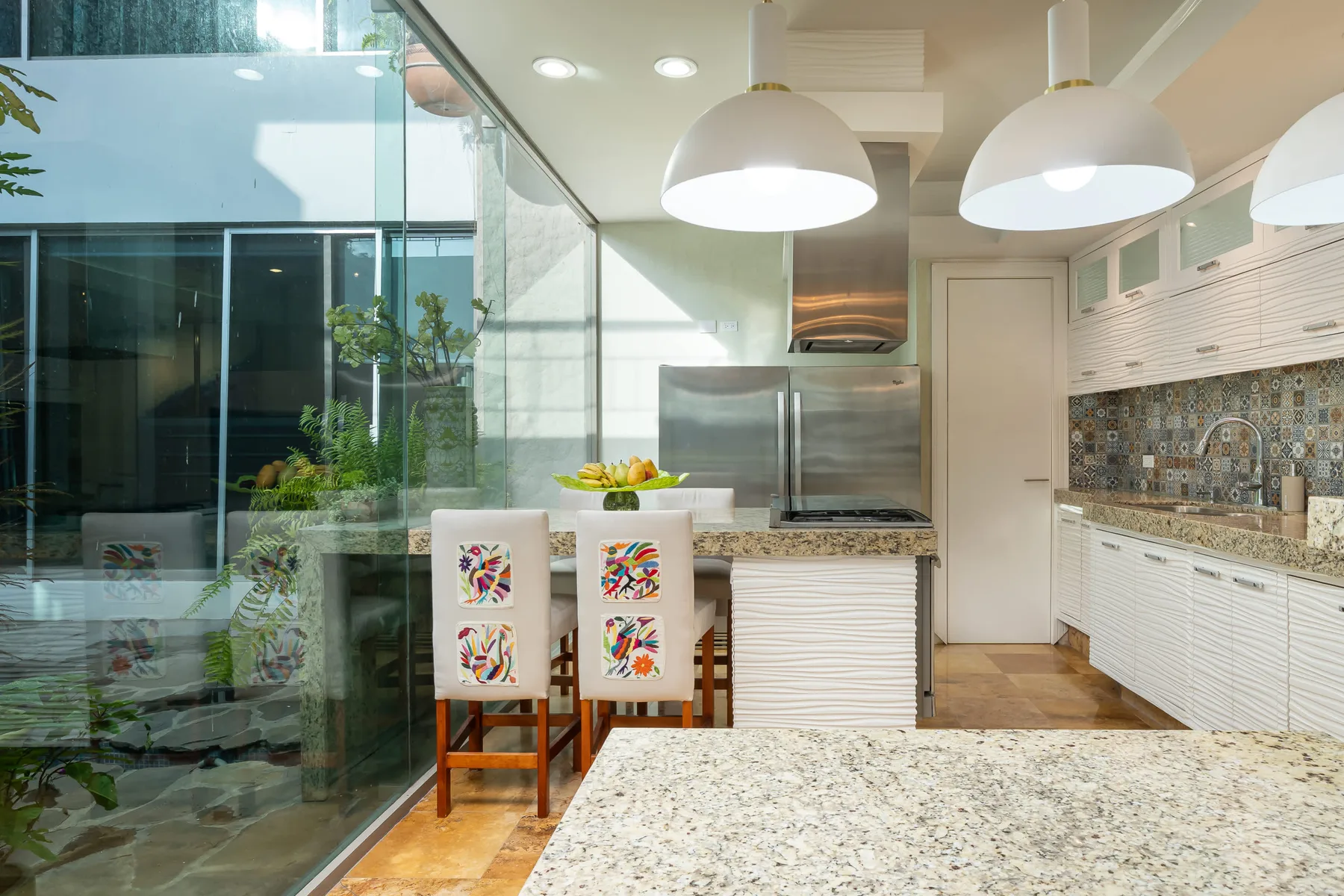 Una cocina luminosa con una barra y asientos estampados junto a una pared de vidrio.