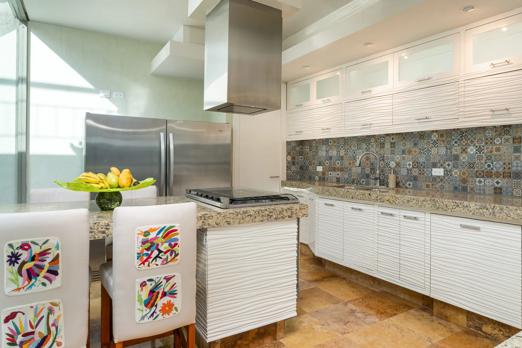 Una cocina luminosa con gabinetes blancos, un salpicadero de azulejos y una isla central.