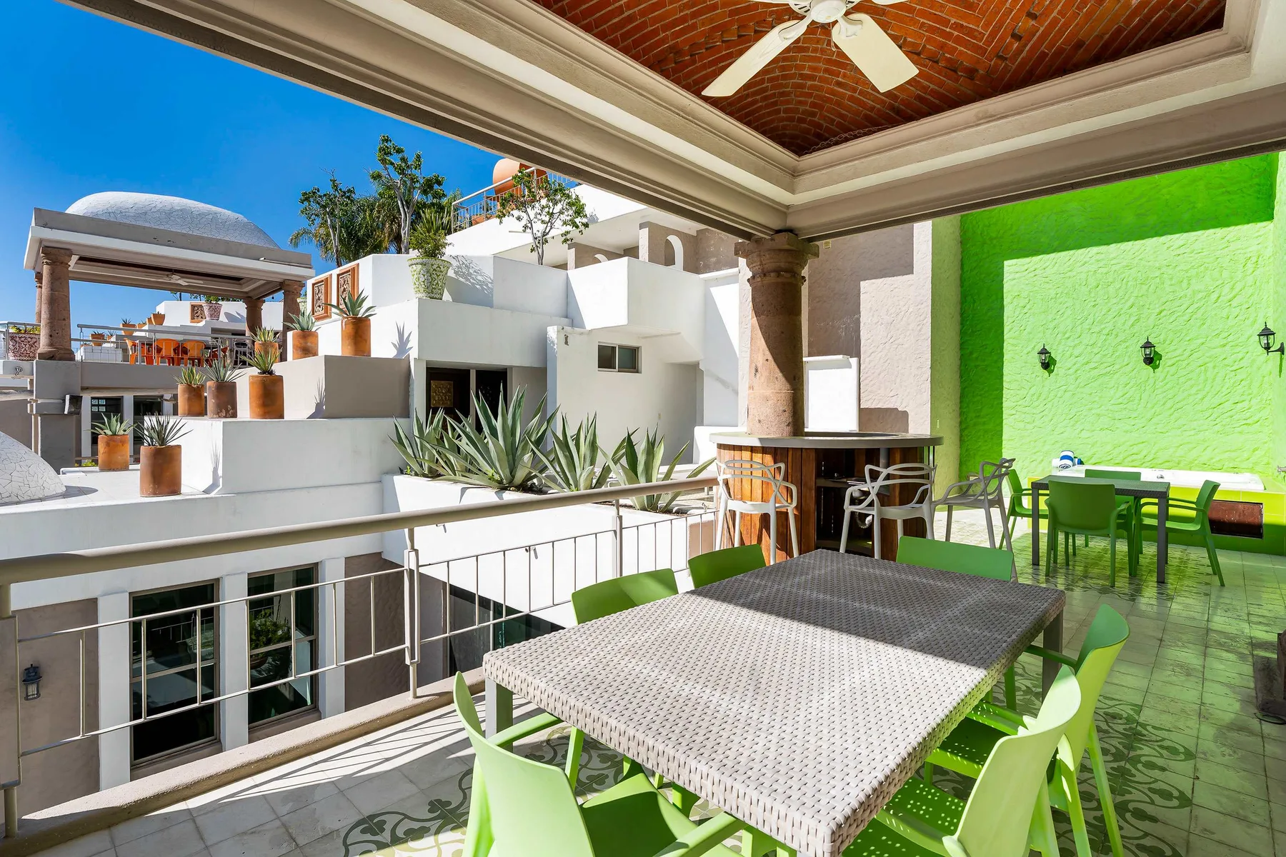 Una terraza comedor al aire libre con sillas verdes y una mesa bajo un techo.