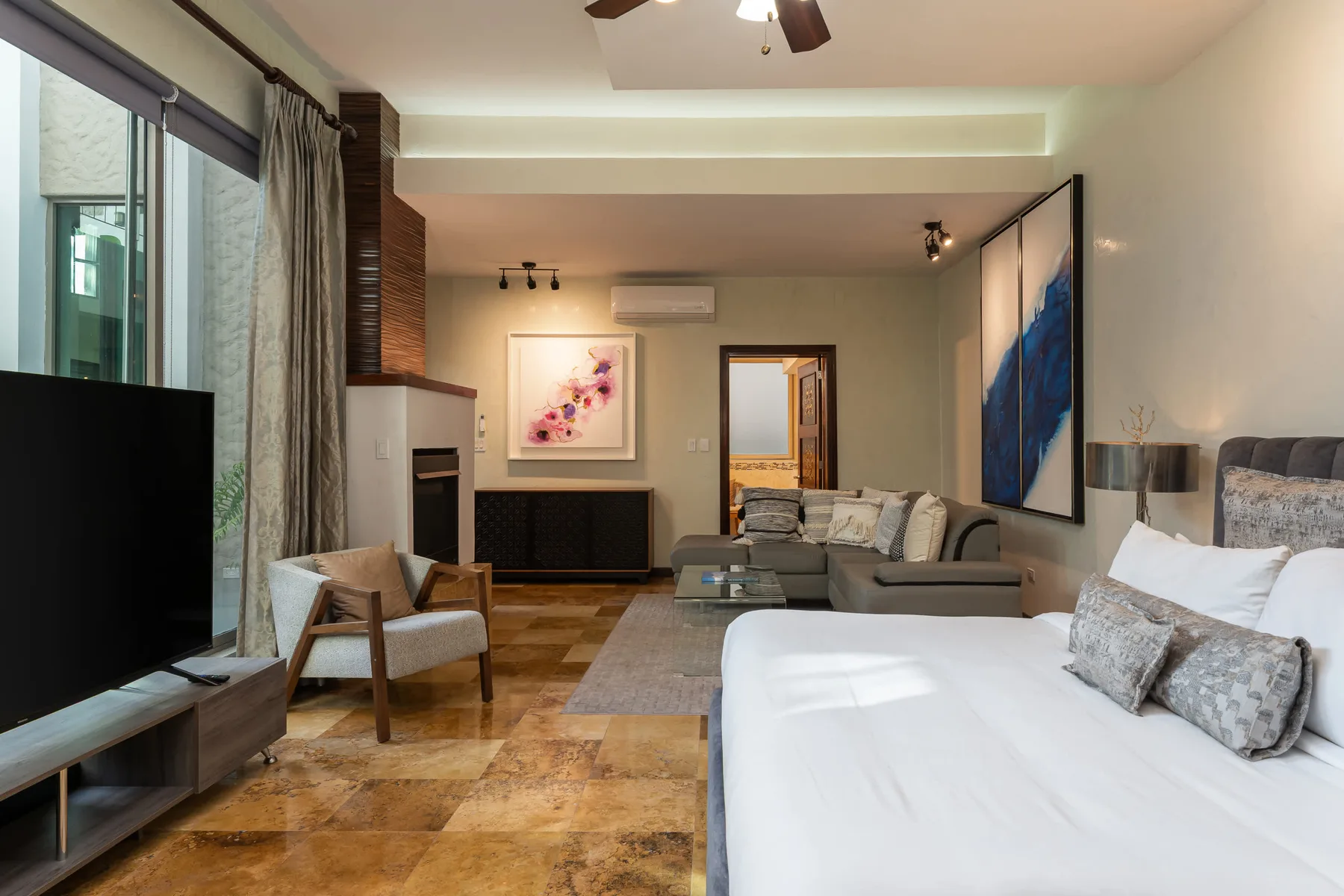 Un dormitorio con zona de estar, cama, asientos y grandes ventanas.